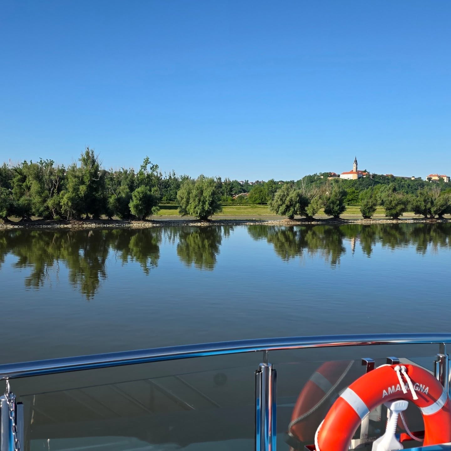Trees and a church reflected in the Danube beside an AmaMagna life ring