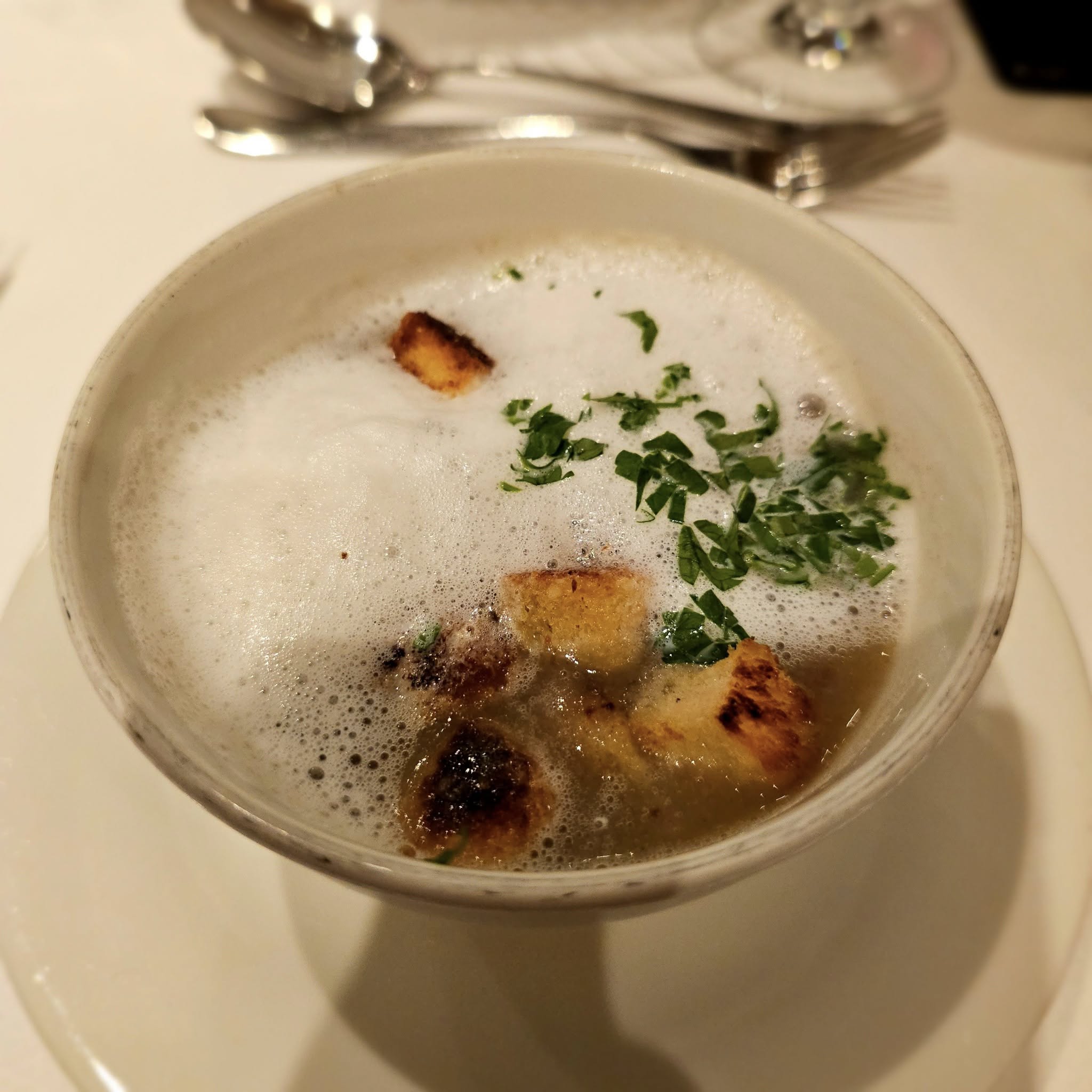 A bowl of soup with croutons and herbs on AmaSonata