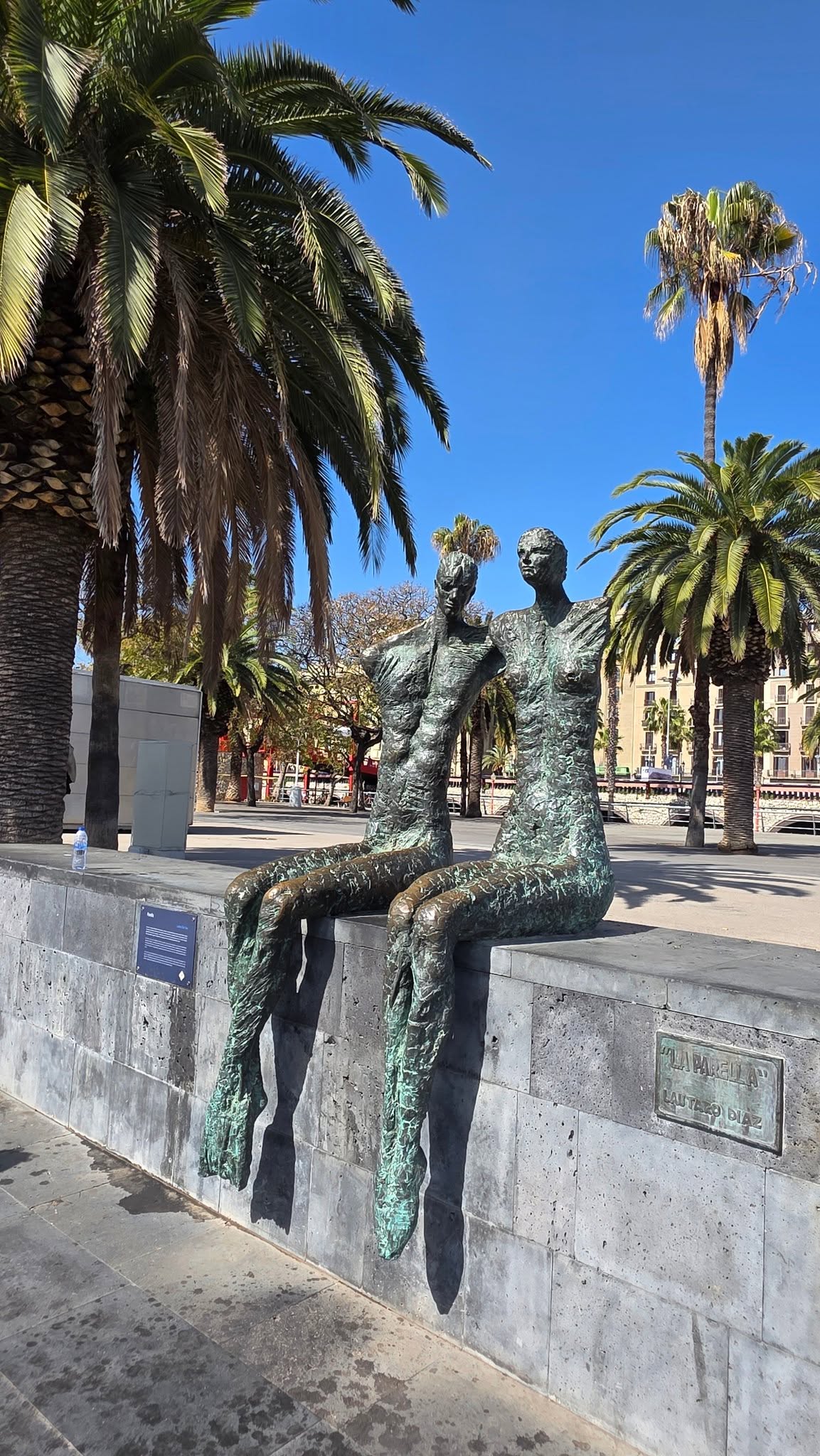 Two seated bronze figures beside the Barcelona waterfront