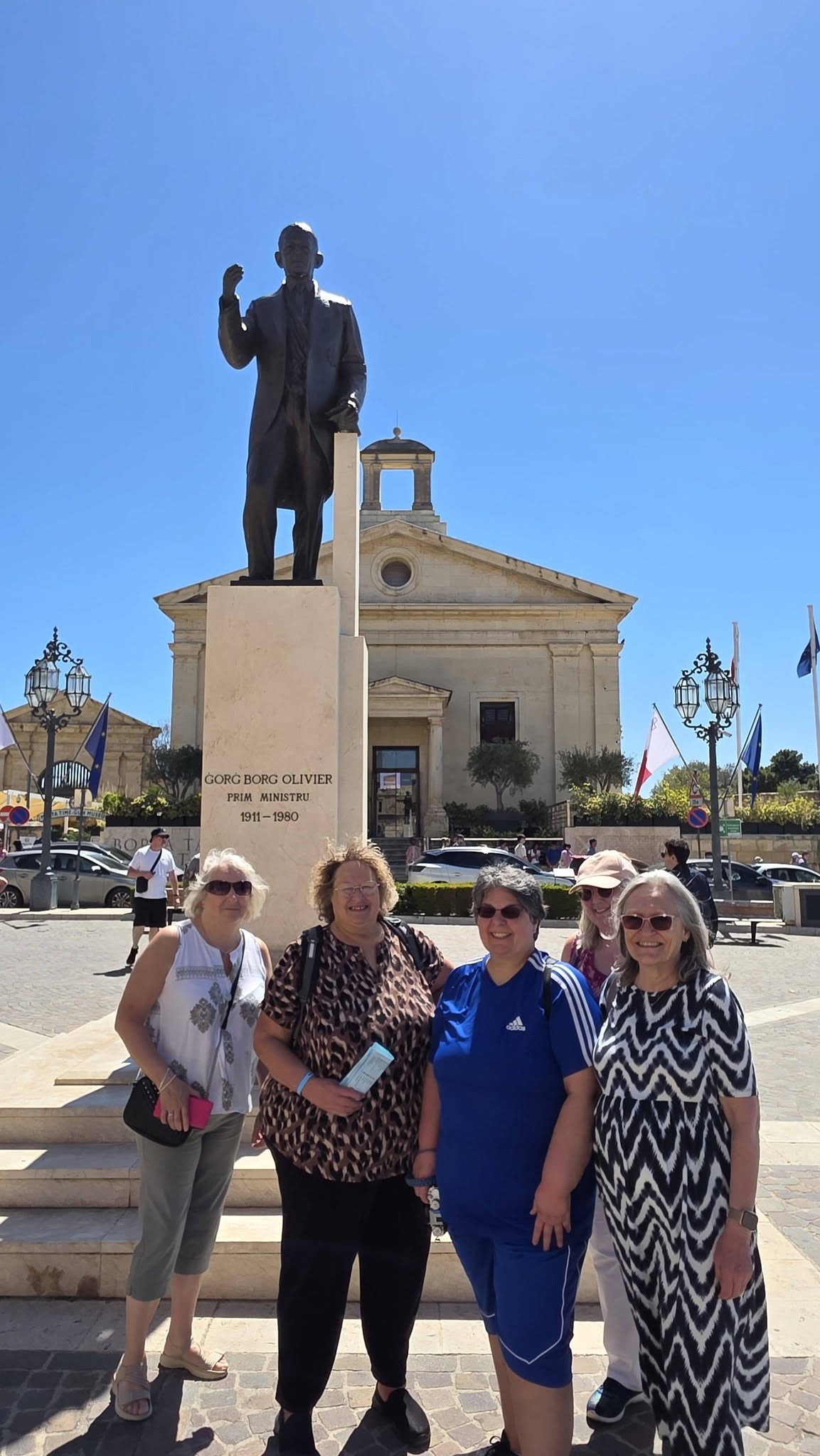 Four solo travellers together beside a statue in a sunny square in Malta