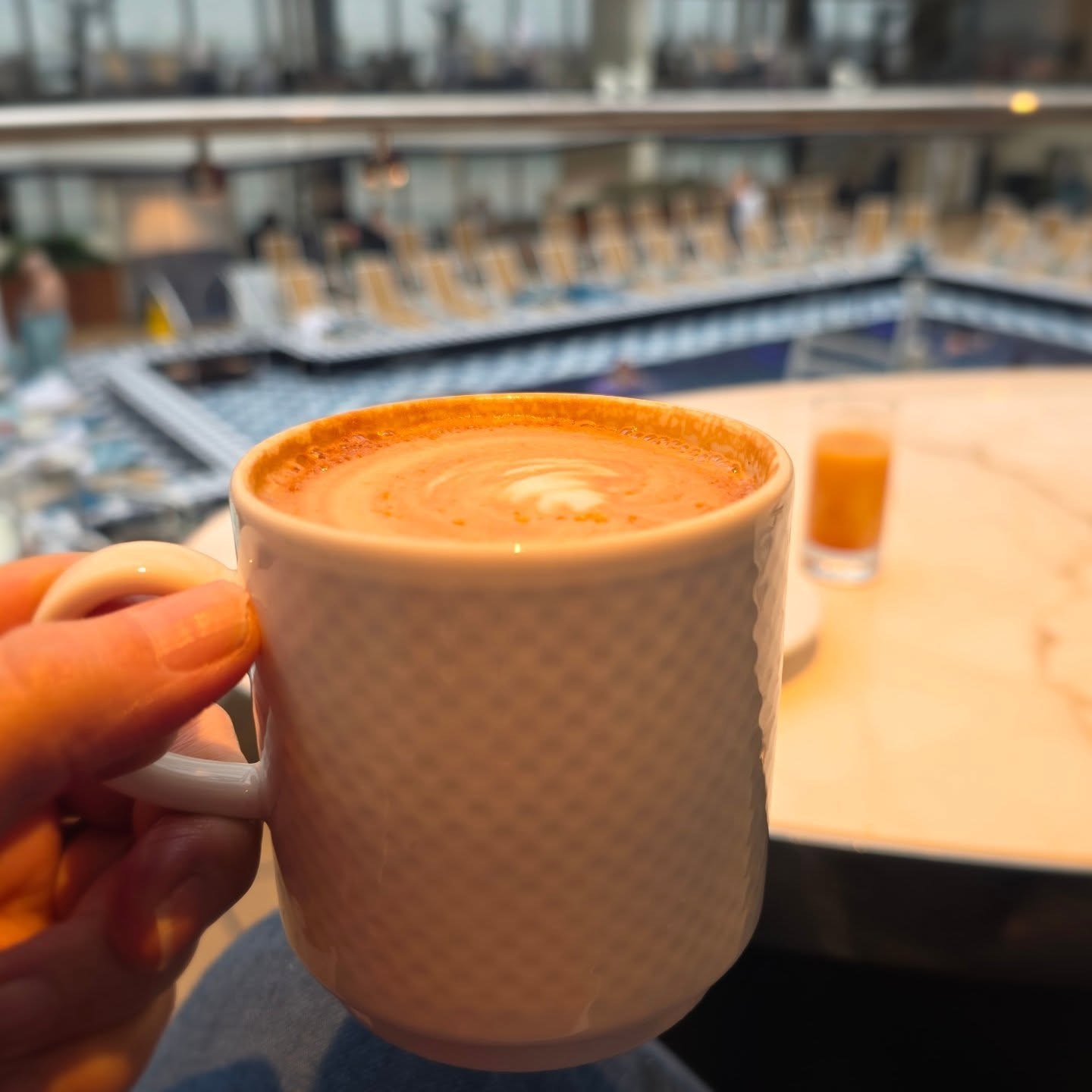 A hand holding a coffee with the café in the background