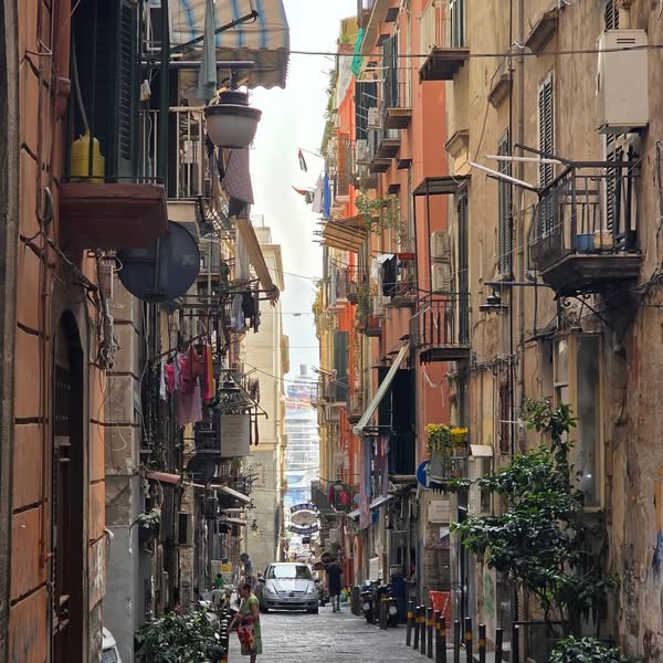 Narrow colourful Naples street, with a cruise ship visible at the distant end.