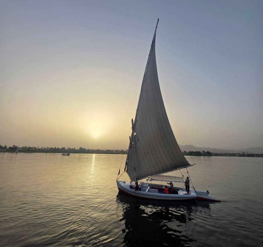 A felucca sailing on the Nile with the sun setting behind it