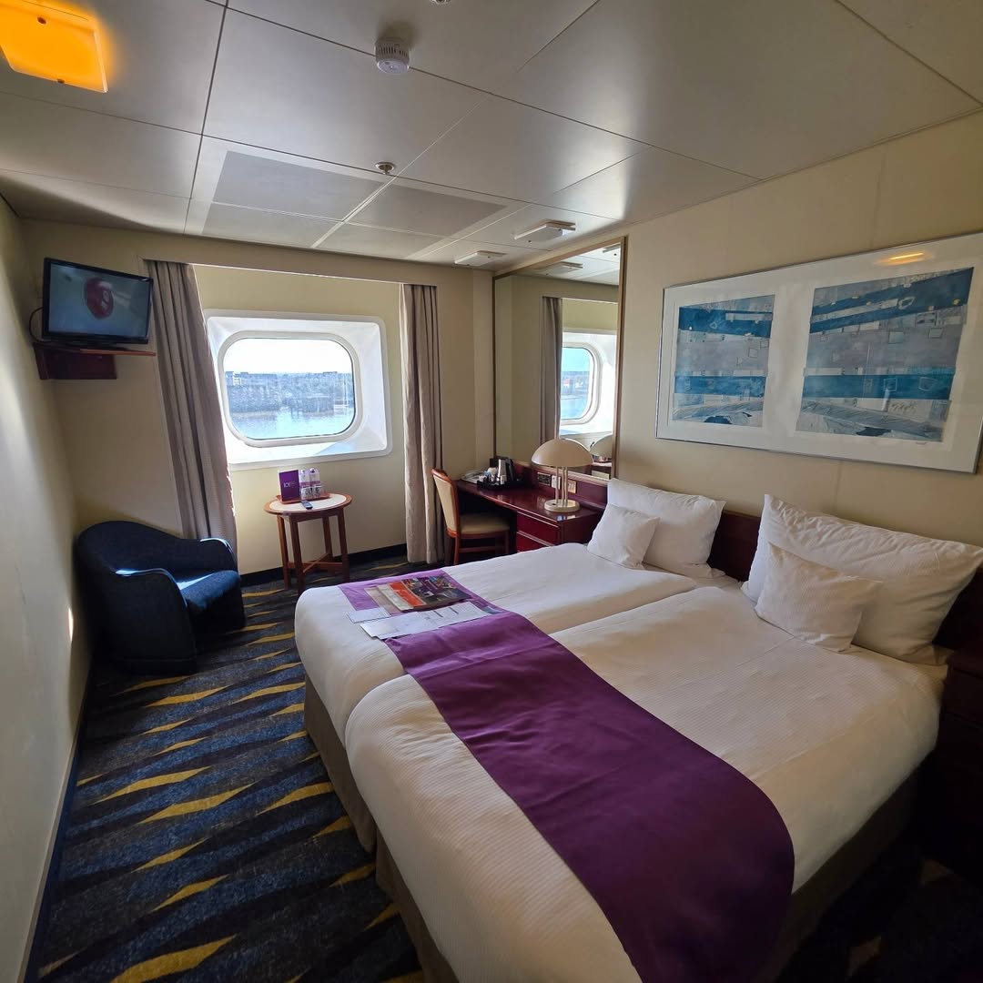 Oceanview cabin with twin beds, purple runners and two windows.